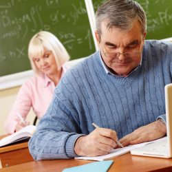 Senior man in eyeglasses carrying out written task in classroom