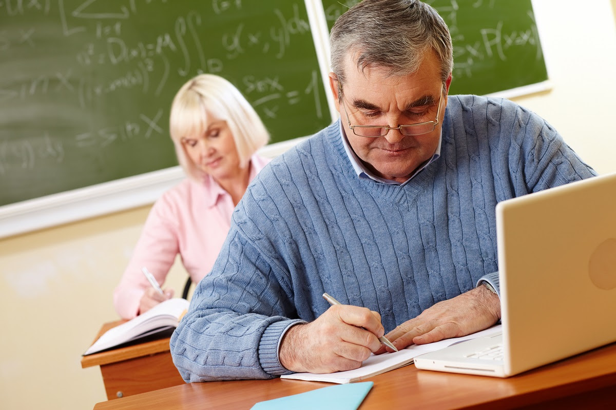 Senior man in eyeglasses carrying out written task in classroom